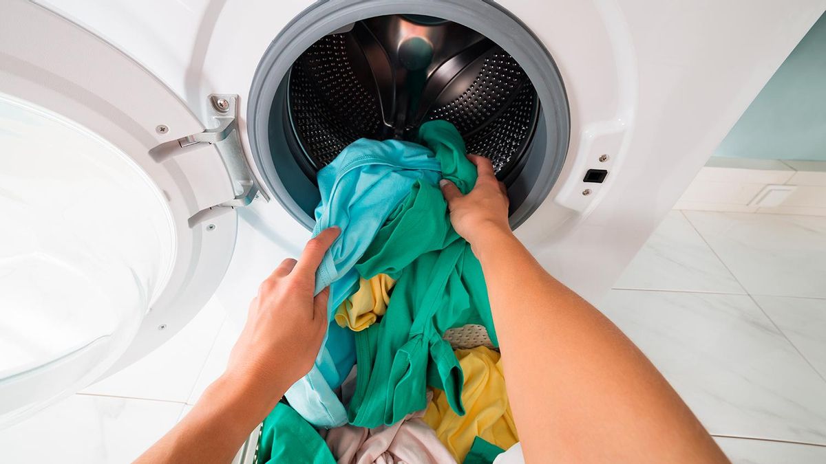 hands putting colored clothes into the washing machine